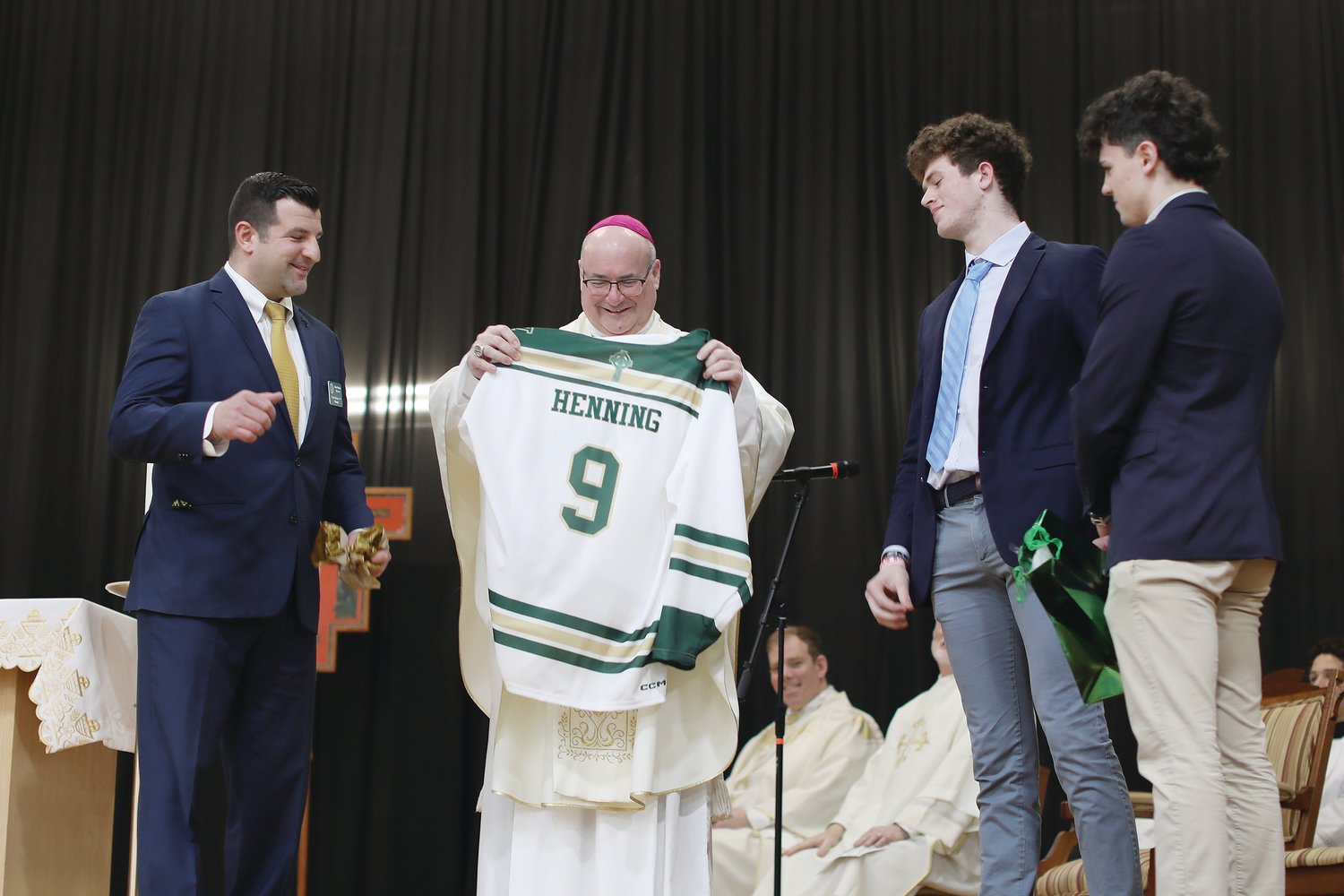 Coadjutor Bishop Richard G. Henning visits Bishop Hendricken High School on Friday, March 3. Pictured: Heis presented with a school jersey by Principal Mark DeCiccio ‘03, and student athletes Alexander Clemmey ‘23 and Steven Nardelli ‘23.